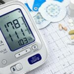 Cyfrowy ciśnieniomierz z wydrukiem EKG obok tabletek i narzędzi medycznych